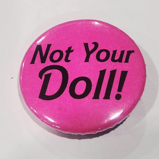 Pink button with 'Not Your Doll!' text on a white background