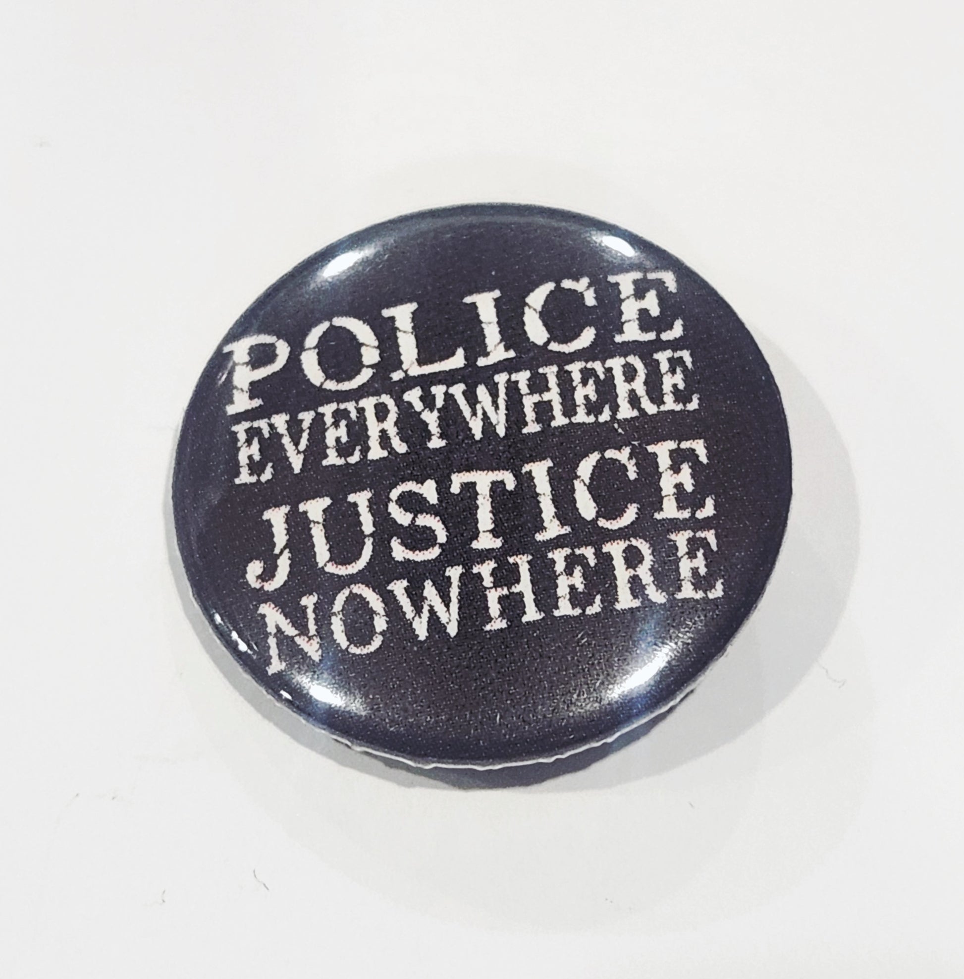 Button badge with 'POLICE EVERYWHERE JUSTICE NOWHERE' text on a black background